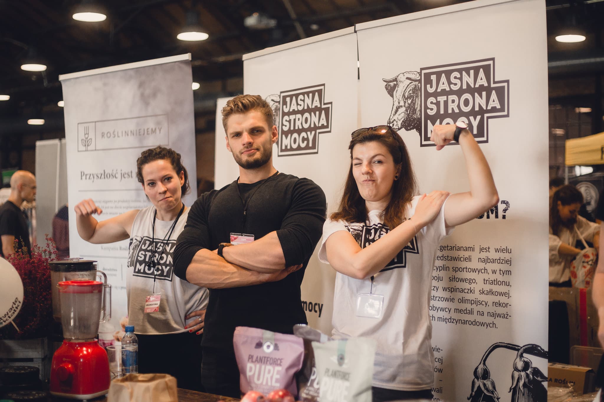Aktywiści na stoisku Jasnej Strony Mocy prężą muskuły, pokazując siłę na wegańskiej diecie.